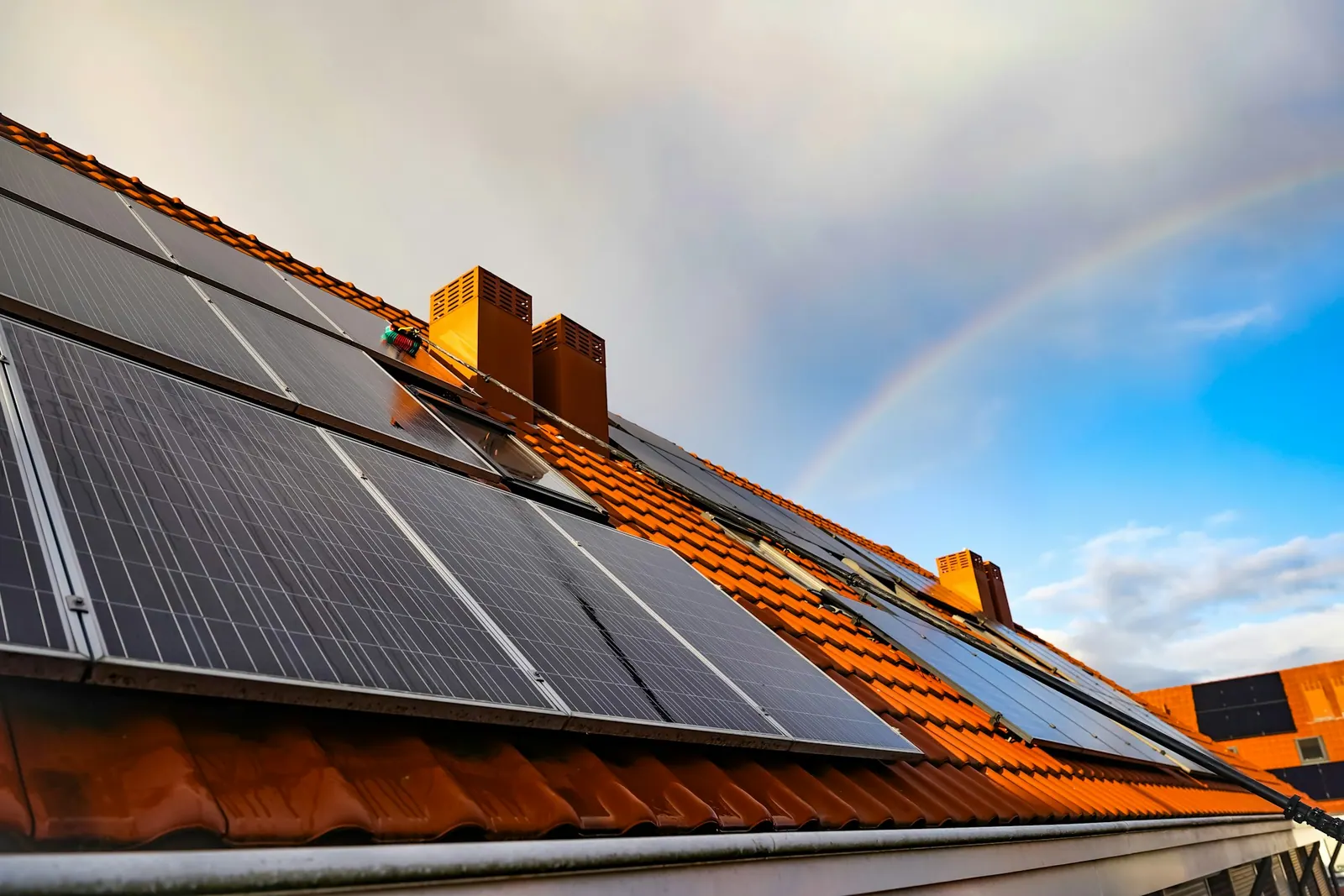 Rooftop solar panels with a rainbow behind them after rain